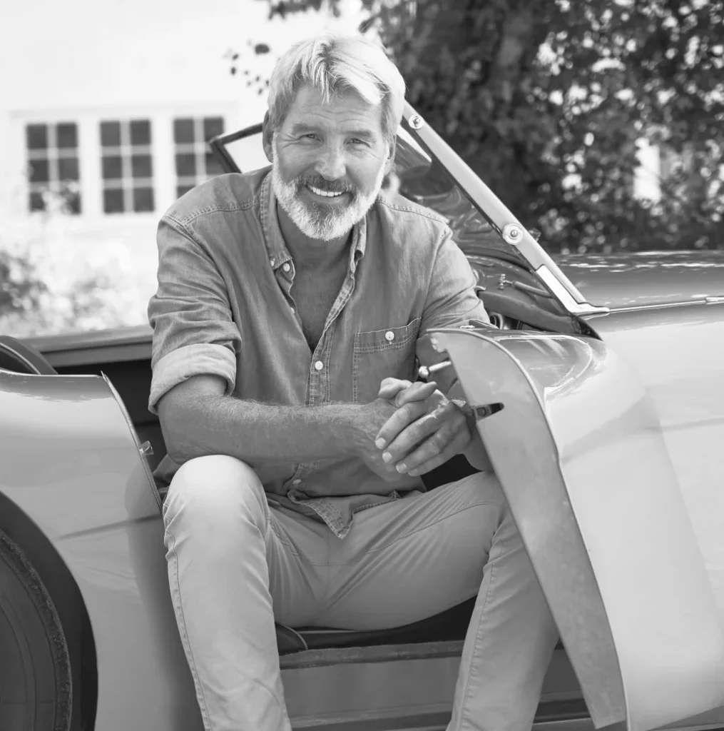 Smiling man sitting in a classic car, in black and white